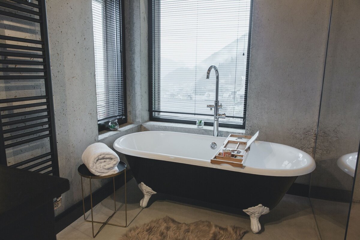 A bathtub in a bathroom next to a window with blinds