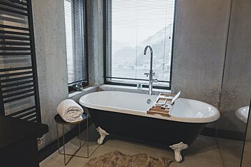 A bathtub in a bathroom next to a window with blinds