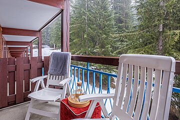 A chair with a blanket on it sits on a balcony overlooking a snowy forest