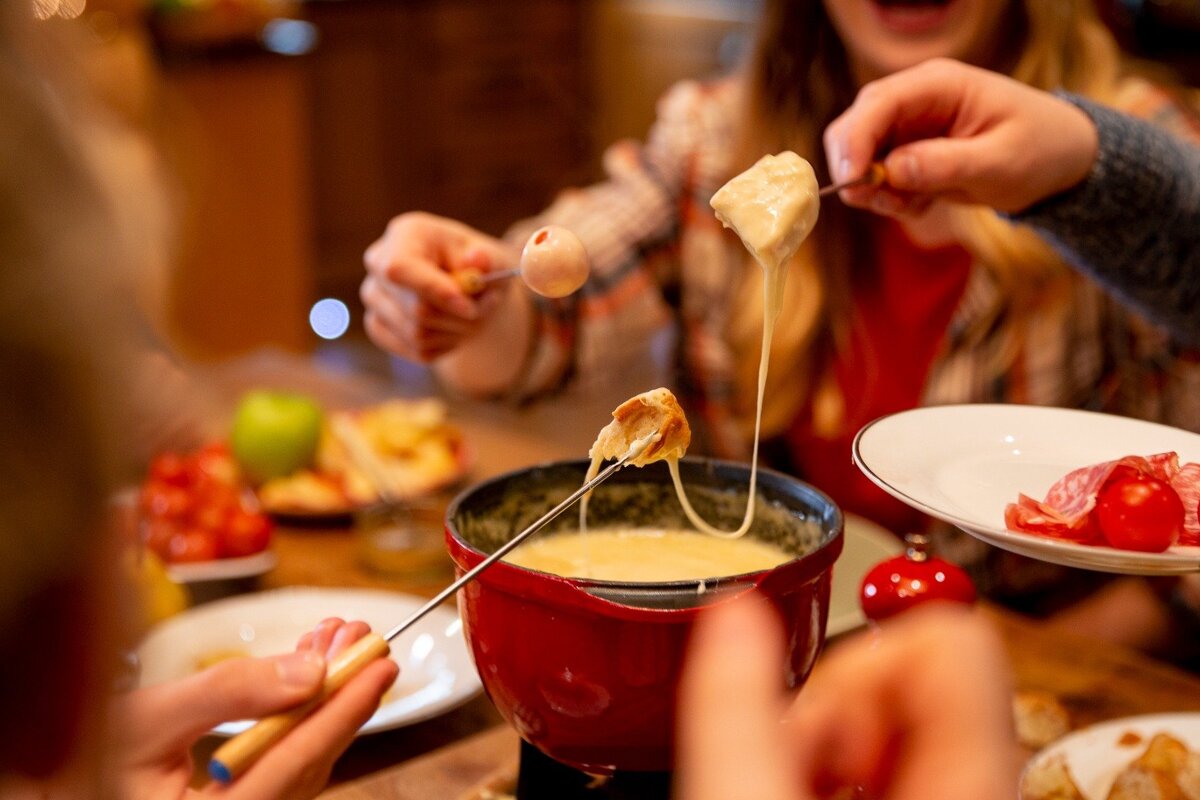 A person dipping a piece of meat into a fondue pot