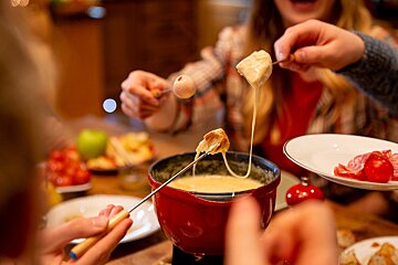 A person dipping a piece of meat into a fondue pot