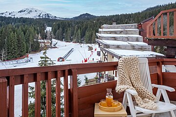 A chair with a blanket on it sits on a balcony overlooking a ski slope