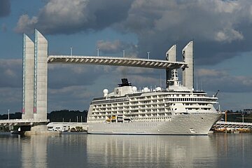 A large white cruise ship is docked under a bridge
