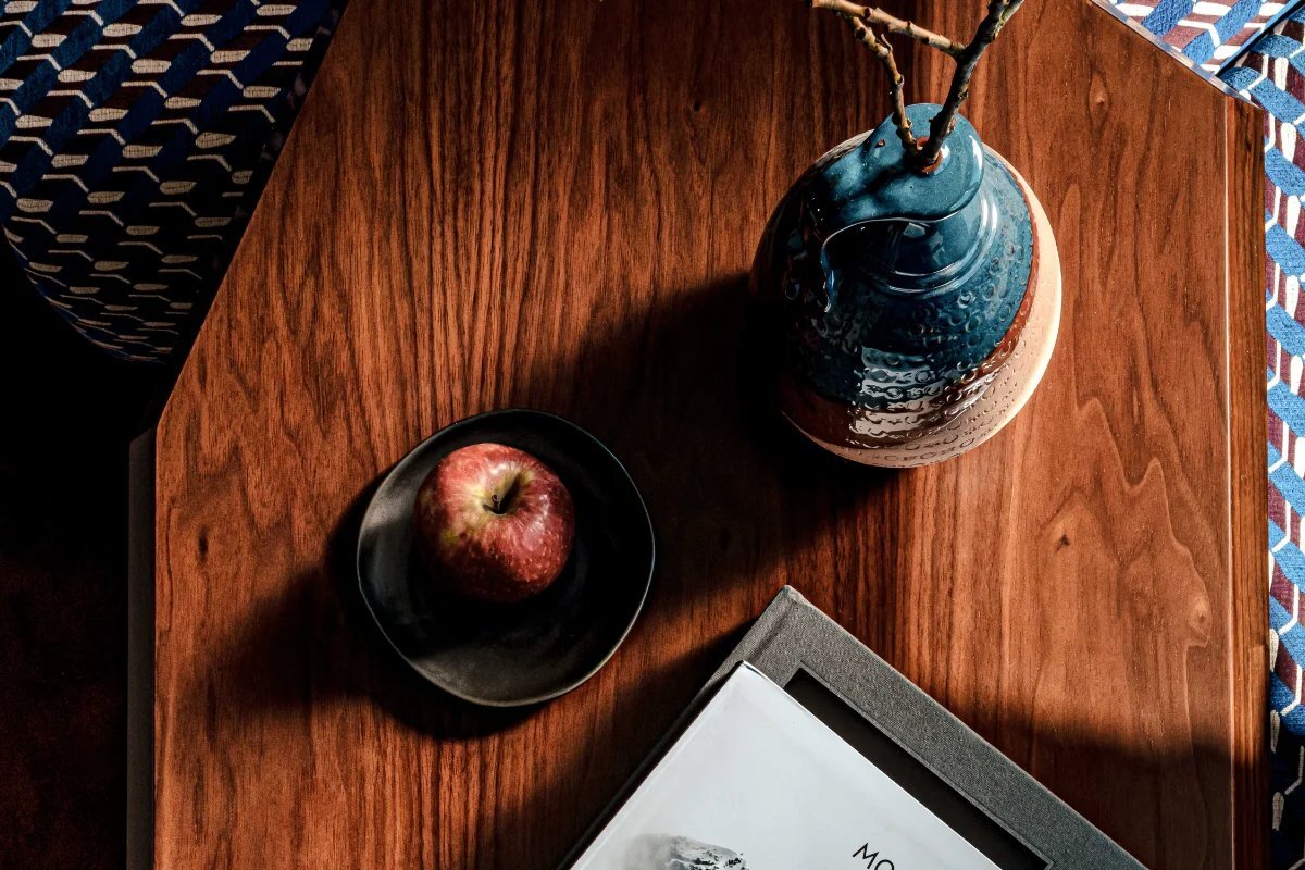 An apple sits on a wooden table next to a book and a vase