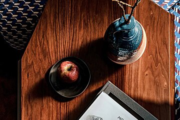 An apple sits on a wooden table next to a book and a vase