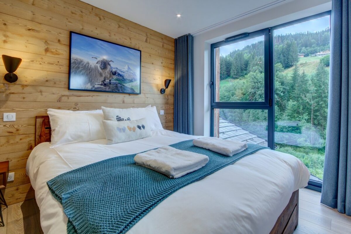 A bedroom with a large window and a painting on the wall above the bed