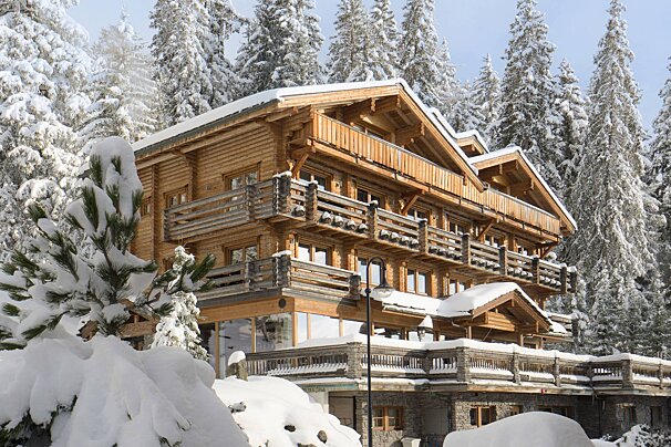 A large log cabin is surrounded by snow covered trees