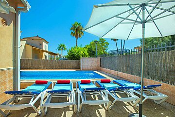 A row of lounge chairs sit under an umbrella in front of a swimming pool