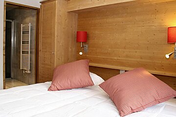 A bedroom with wood paneling and two red lamps on the wall