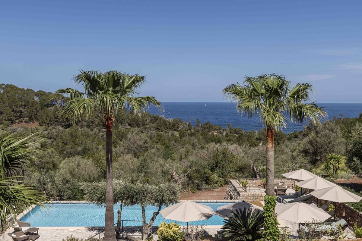 A swimming pool surrounded by palm trees and umbrellas overlooking the ocean