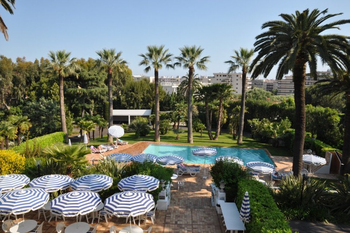 A swimming pool surrounded by palm trees and blue and white striped umbrellas