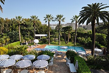 A swimming pool surrounded by palm trees and blue and white striped umbrellas