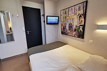 A small bedroom with a painting on the wall above the bed