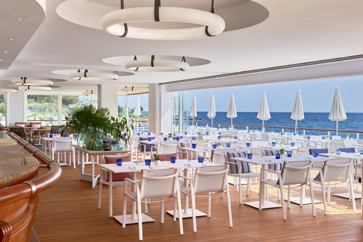 A restaurant with tables and chairs and umbrellas overlooking the ocean