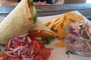 A wrap sandwich with tomatoes , onions , and coleslaw on a plate with tortilla chips