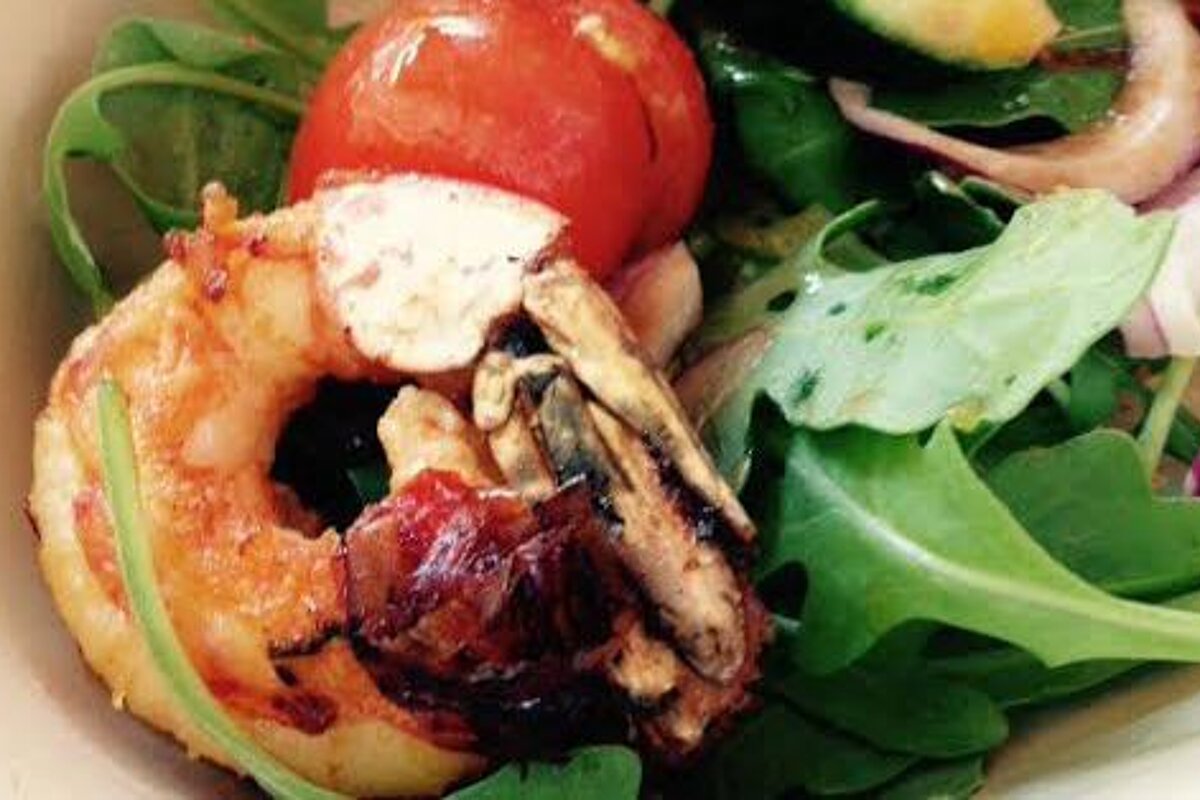 A close up of a salad with shrimp , mushrooms , and tomatoes in a bowl