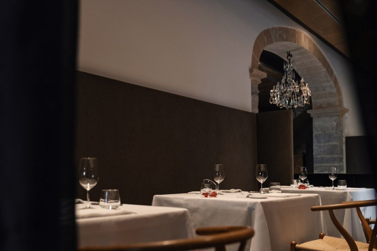Elegant restaurant with white-clothed tables, wine glasses, and a sparkling crystal chandelier hanging from a stone archway, creating a sophisticated ambiance.