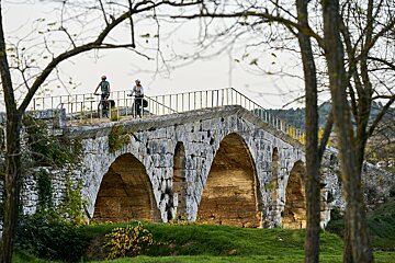 Two people riding bicycles on a stone bridge