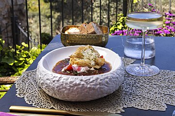 A bowl of food sits on a table next to a glass of wine