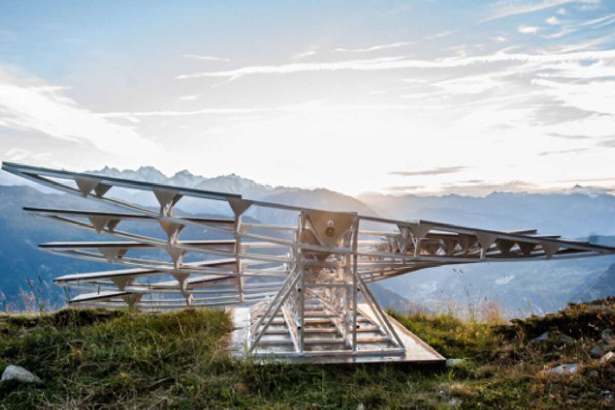 A metal structure on top of a grassy hill with mountains in the background
