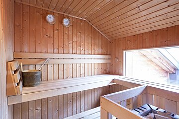 A wooden sauna with a bucket and a thermometer on the wall