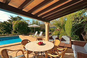 A table with a bowl of apples on it sits on a patio next to a pool