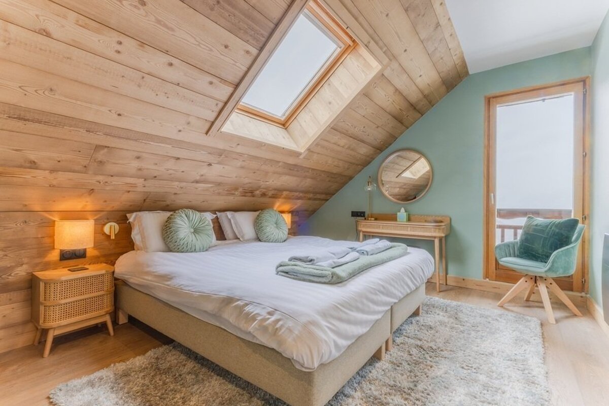 Cozy attic bedroom with a sloped wood-paneled ceiling, skylight, large bed with green cushions, and matching green decor.