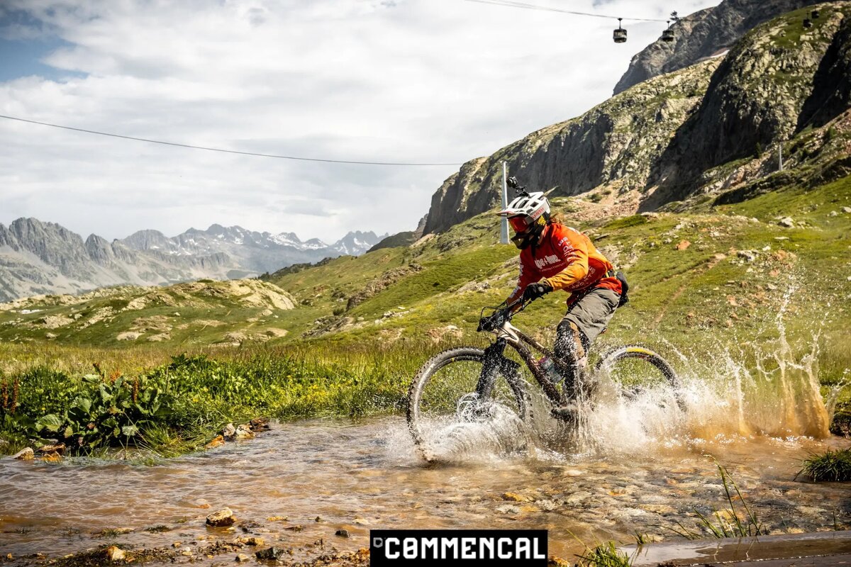 A person riding a bike through a stream with the word commencal on the bottom