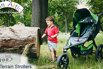 A boy standing next to a stroller that says all terrain stroller