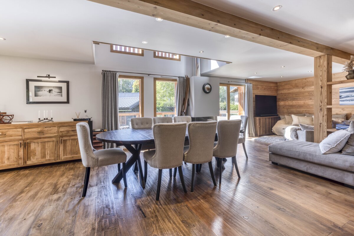 Spacious, rustic-modern open-plan living and dining room with wooden floors, large windows, a dark dining table, and cozy lounge seating.