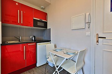 A small kitchen with red cabinets and white chairs