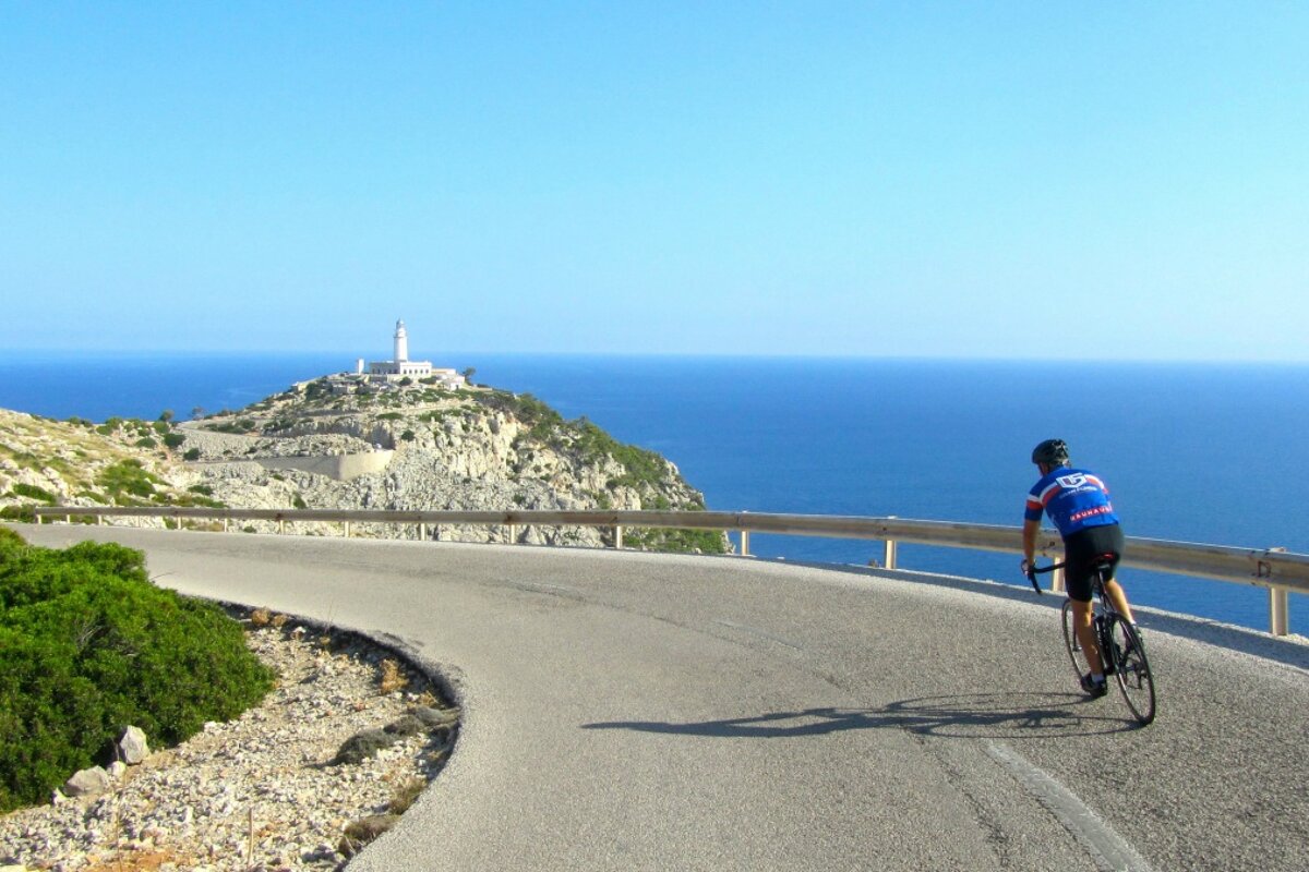 A person riding a bike on a road with a lighthouse in the background