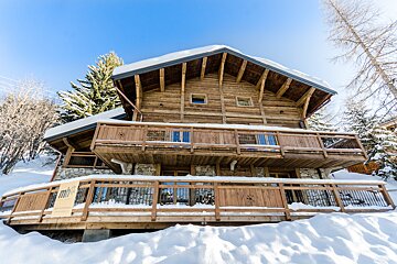 A large wooden house is surrounded by snow and trees