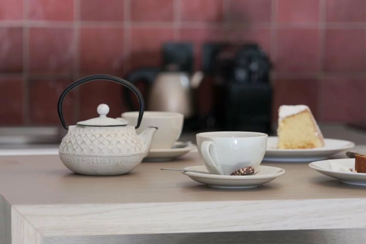 A table with a teapot and cups and saucers and a piece of cake