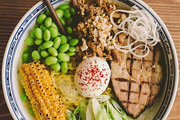 A bowl of ramen with corn on the cob and a hard boiled egg