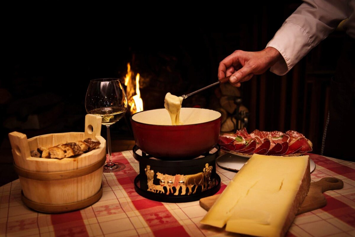 A person is dipping a piece of cheese into a fondue pot
