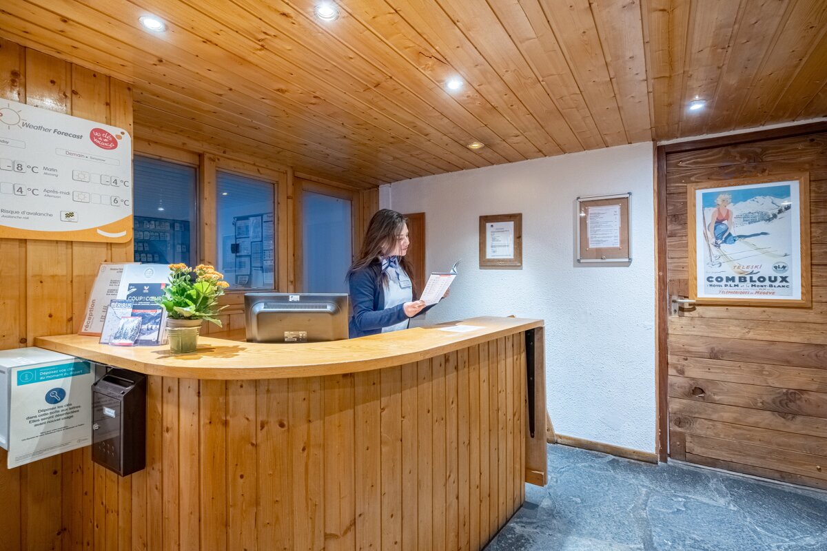 A woman stands behind a wooden counter in front of a sign that says combloux