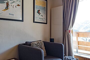 A chair in front of a window with a meribel poster on the wall above it
