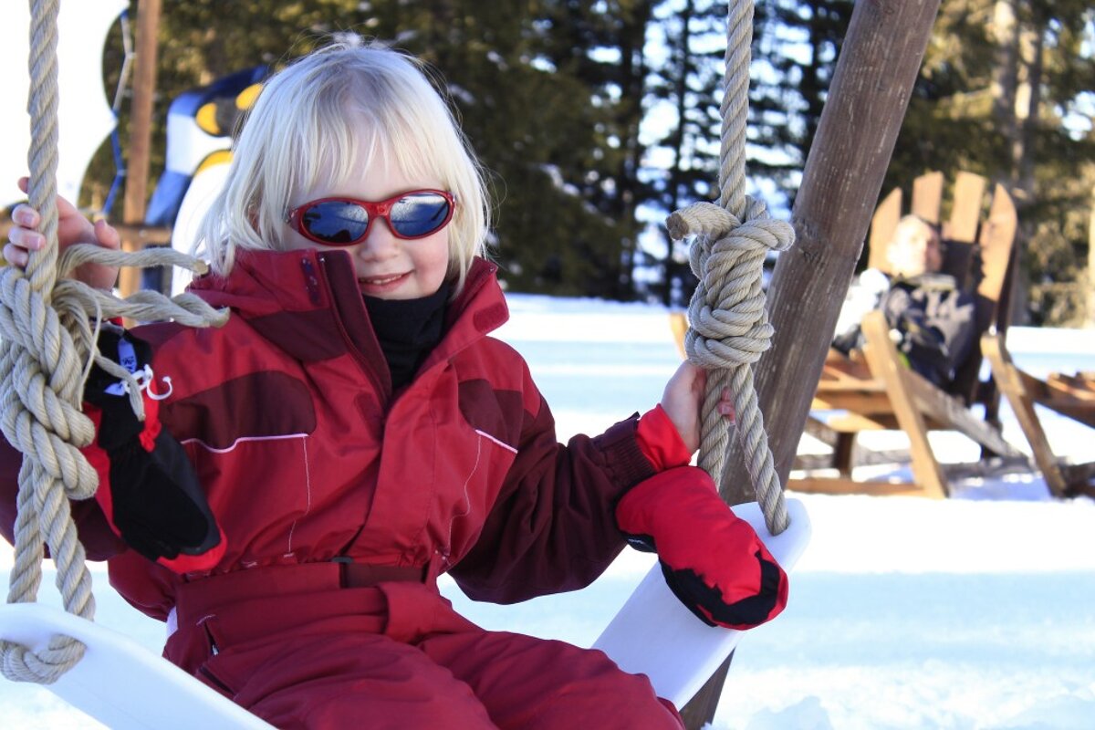 a child on a swing in sunglasses and a ski outfit