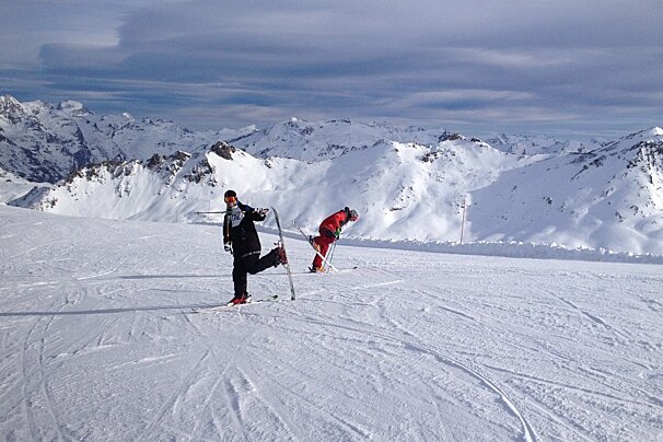 Two people skiing on a snowy slope with mountains in the background