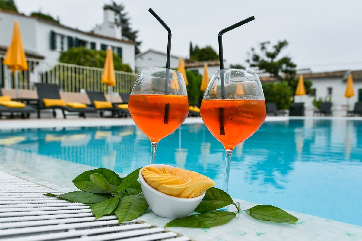 Two glasses of orange drinks next to a swimming pool