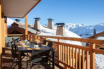 A table and chairs on a balcony overlooking snow covered mountains