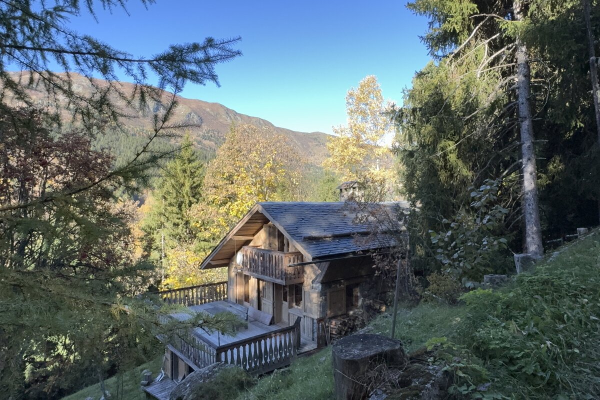 A rustic wooden cabin with decks, surrounded by vibrant autumn foliage and mountains under a clear blue sky.