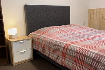 A bedroom with a bed and a nightstand with a lamp on it