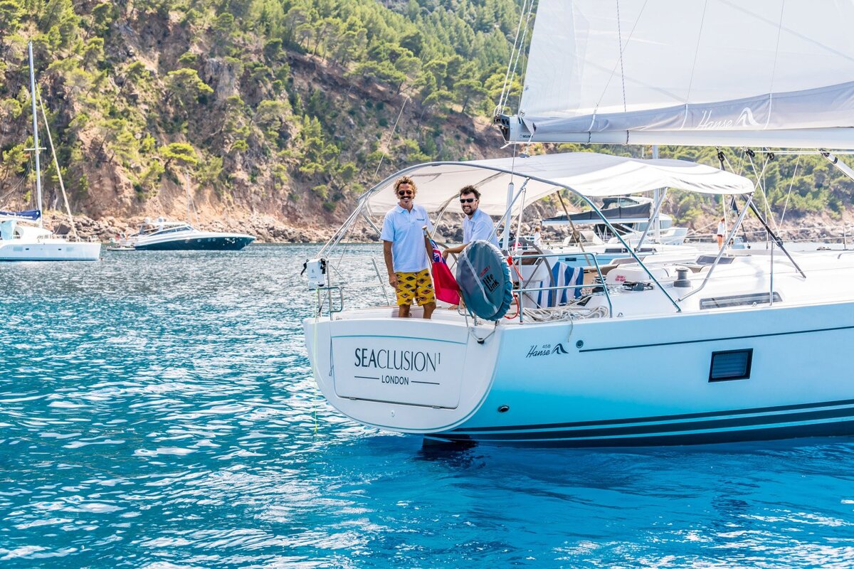 Two men stand on a white sailboat,