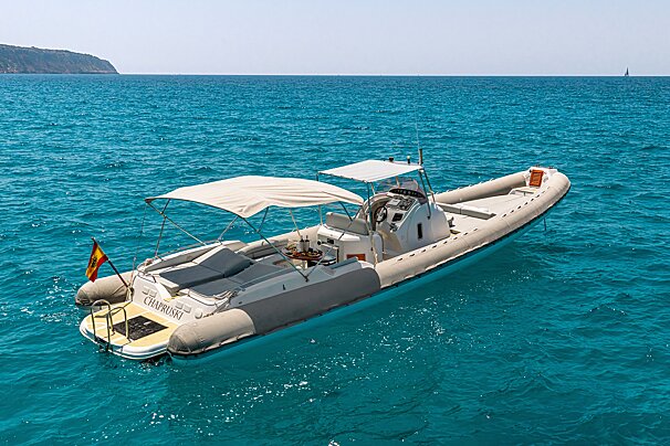 A luxury rigid inflatable boat with a canopy floats on clear, vibrant turquoise water under a bright sky.