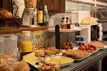 A vibrant breakfast buffet display with orange juice, cheese, baked goods, fruit, cereals, eggs, and tomatoes on a tiled counter.