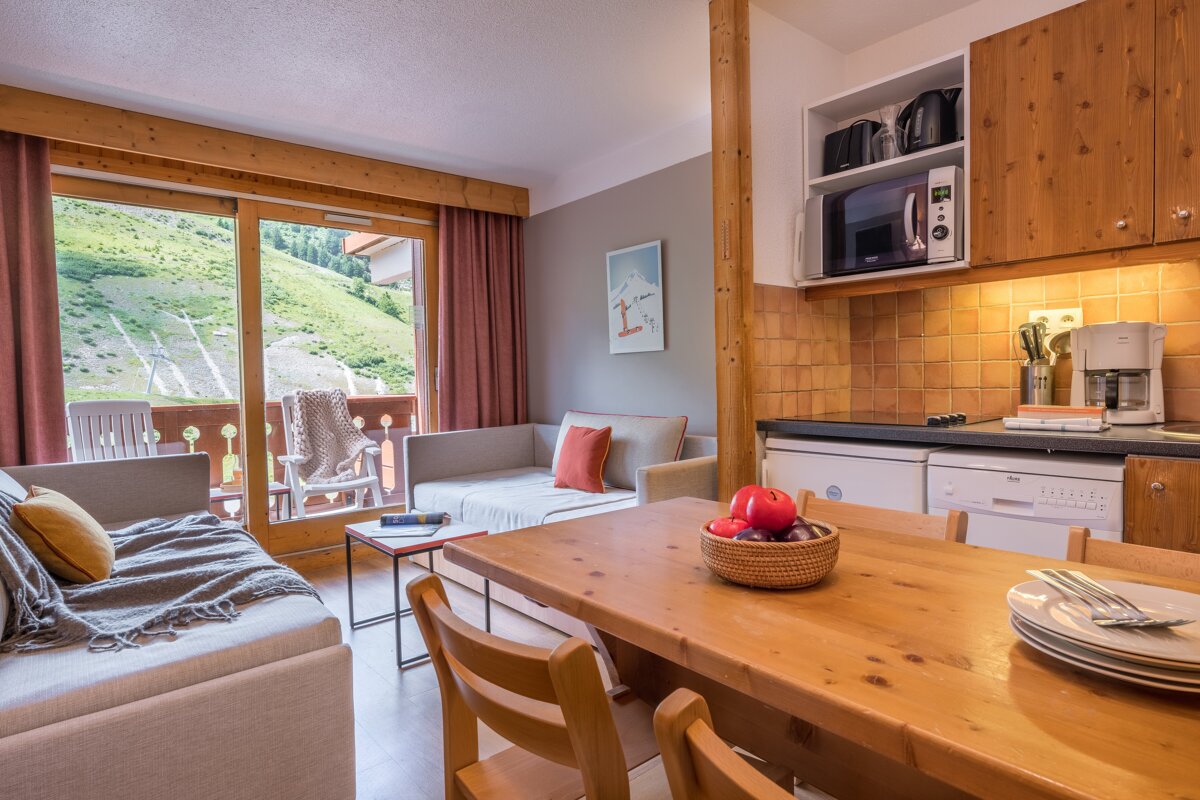 A cozy apartment with a combined living/kitchen area, wooden accents, sofas, and a balcony offering a scenic green mountain view.