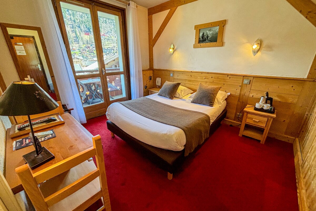 A hotel room with a bed a desk and a lamp