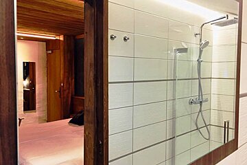 A bathroom with a shower and a bed in the background